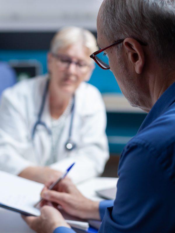 Old Man Signing Appointment Papers For Healthcare System At Checkup Visit