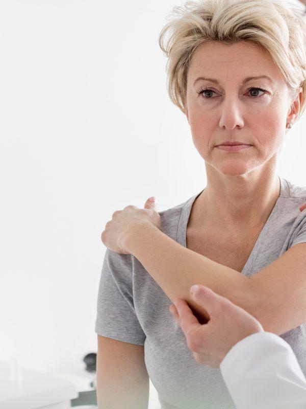 Doctor Assisting Mature Patient In Stretching Her Arm At Hospital